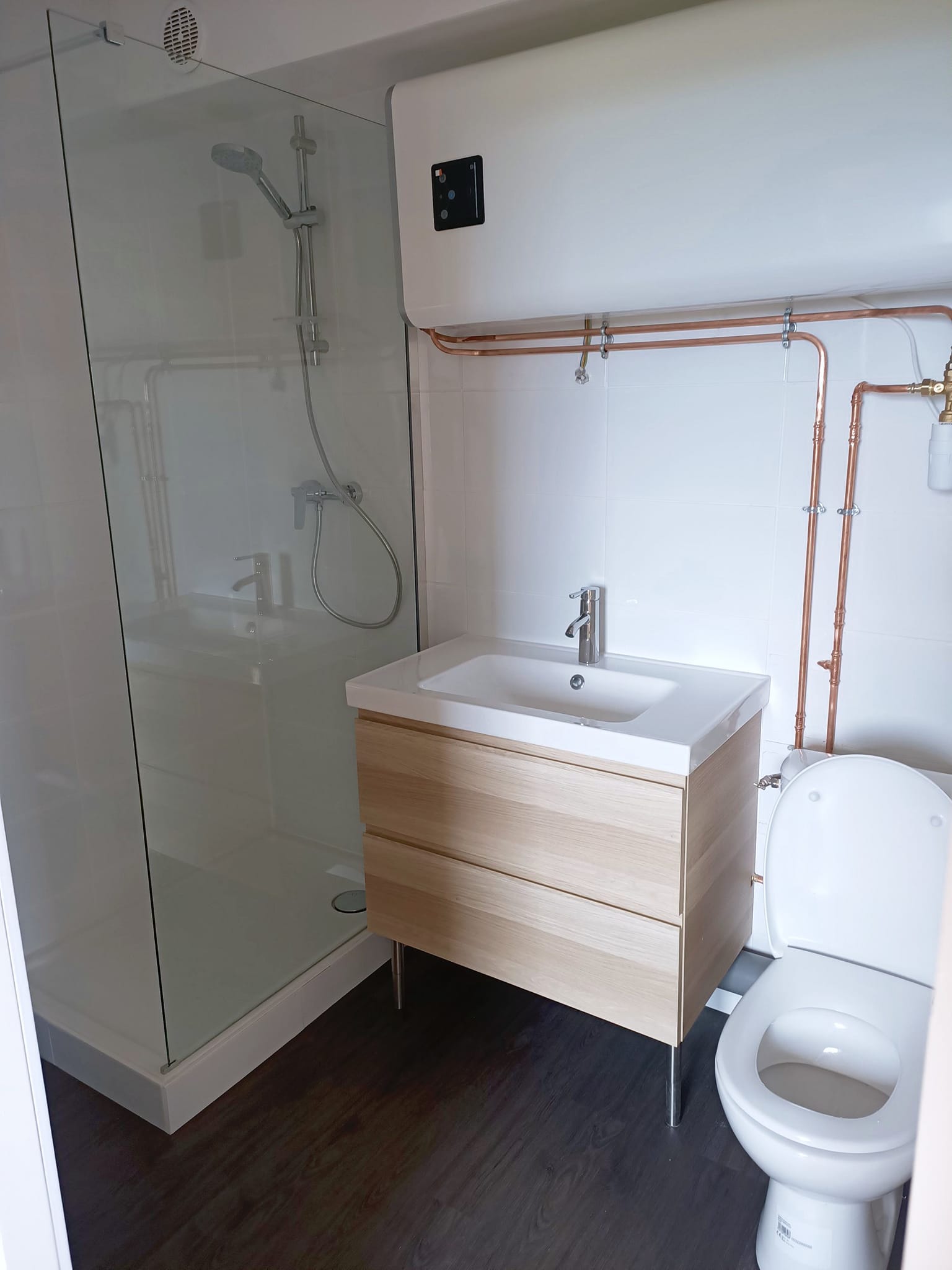 Salle d'eau finie : douche, meuble vasque, WC et chauffe-eau apparent