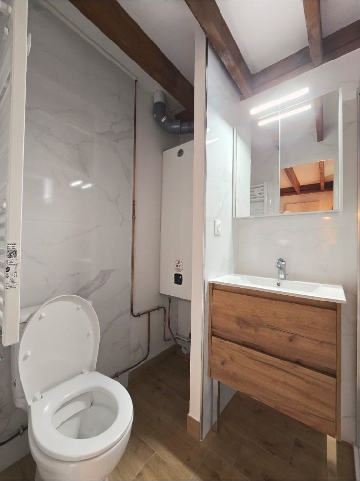 Salle d'eau rénovée : carrelage marbre, meuble vasque chêne, WC neuf et poutres apparentes mises en valeur
