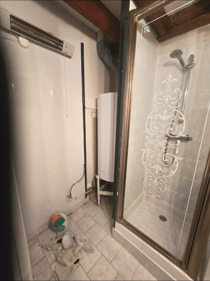 Salle d'eau vétuste sous combles avant rénovation : ancien carrelage et installations à reprendre